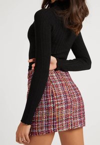 Sort ribbet rullekravesweater med lange ærmer, kombineret med en flerfarvet tweed mininederdel med et struktureret ternet mønster.