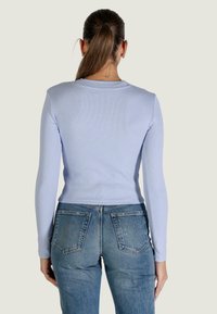 Top a maniche lunghe azzurro chiaro a coste abbinato a jeans a vita alta di colore blu sbiadito. La vestibilità è aderente, con una scollatura delicata.