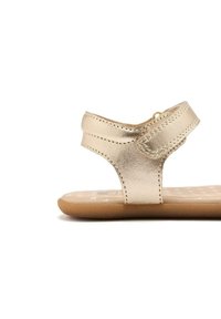 Sandalias con un revestimiento texturizado en dorado metálico, con una correa curvada y cierre de velcro. Suela marrón con patrones de estrellas.