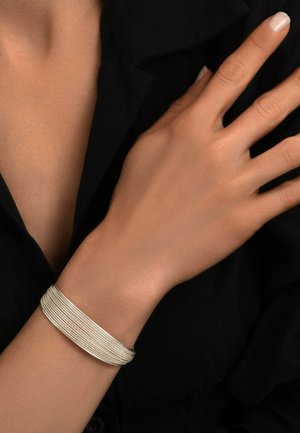 Bracelet en argent avec plusieurs brins texturés, bords lisses et design minimaliste, porté sur un poignet contre un fond sombre.