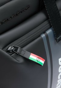 Borsa nera con superficie testurizzata, dotata di cursore della cerniera multicolore che mostra la bandiera italiana e marchio in rilievo sul materiale.