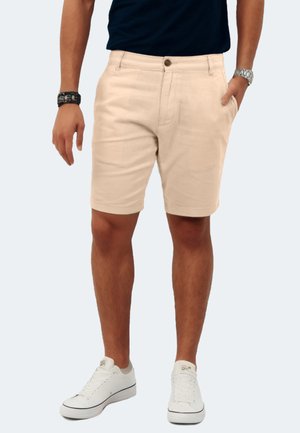 Beige cotton shorts with a regular fit, mid-rise waist, front pockets, and detailed stitching. Paired with white sneakers.