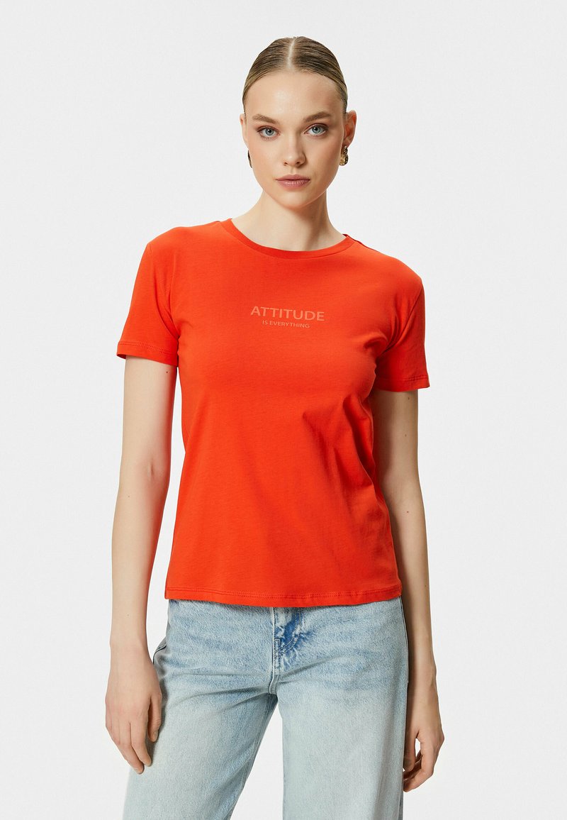 Camiseta roja de manga corta en algodón suave con cuello redondo. Presenta la inscripción "LA ACTITUD ES TODO" impresa en beige claro en la parte frontal.