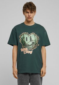 Mørkegrøn bomulds t-shirt med et stort grafisk tryk af et hjerte omgivet af vinstokke og teksten "sad boy" i lys orange. Løs pasform.