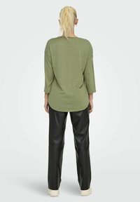 Groen gestreepte blouse met lange mouwen en een ronde zoom, gecombineerd met zwarte leren rechte broek, gedragen met lichtgekleurde sneakers.
