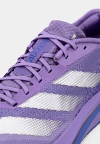 Chaussure de sport violette avec tige en mesh, lacets texturés et trois bandes blanches sur le côté. Dotée d'une semelle rembourrée et d'un détail logo.