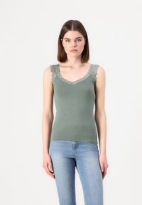 Green tank top with lace trim along the neckline and shoulders, made of soft fabric, paired with light blue fitted jeans.