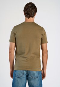 Camiseta de manga corta verde oliva con cuello redondo, textura suave y estilo ajustado. Combinada con pantalones cortos de mezclilla azul claro con bolsillos traseros.