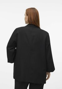 Černý oversize blazer vyrobený z hladkého materiálu, s upraveným límcem, volnými rukávy a čistým designem s minimem akcentů.