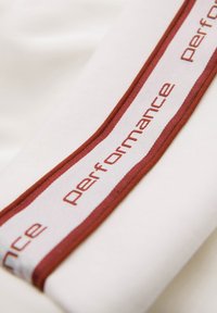 Gros plan d’un tissu blanc avec une bande bordée de rouge présentant le mot répété « performance » en texte rouge.
