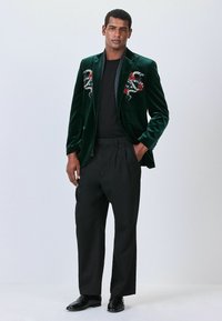 Green velvet blazer with floral embroidery, black t-shirt, loose black trousers, and black shoes. Smooth texture and tailored fit.
