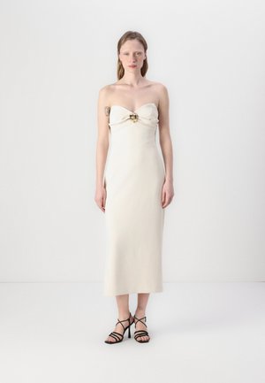 Robe midi sans bretelles de couleur crème avec un devant torsadé et un accent doré. Tissu lisse avec une silhouette ajustée. Portée avec des talons noirs à lanières.
