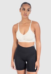 Urheiluliivi vaaleanbeige, jossa on tekstuuripinta ja poimutettu etuosa; yhdistetty korkeavyötäröisten mustien shortsien kanssa. Molemmat ovat joustavia ja myötäileviä.