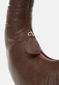 Bota de cuero marrón con una textura suave, con una cremallera lateral y un lazo para fácil manejo. El diseño es elegante y curvado.