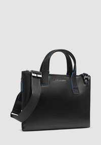 Bolso tote de cuero negro con doble asa y correa para el hombro ajustable. Presenta costuras de acento azul y cierre con cremallera. Textura suave.