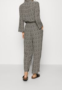 Combinaison à motif noir et blanc avec manches longues, taille ceinturée et coupe décontractée. Présente un design à lignes ondulées et des poches latérales.