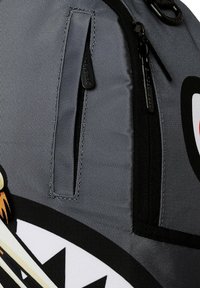 Zaino grigio con una superficie testurizzata, due tasche esterne con zip e un design grafico audace con elementi in bianco e nero.