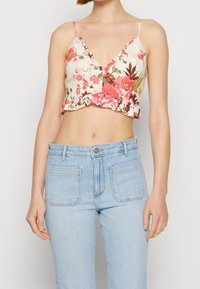 Kukkakirjallinen crop top, jossa on V-kaula-aukko, röyhelöhelma ja ohuet naruoljet. Taustalla on kerma vaalea sävy, jossa on vaaleanpunaisia ja vihreitä kukkakuvioita.