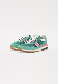 Grønne mokkasinsneakers med lyserøde og marineblå striber, hvide snørebånd, en høj mellem sål og en gummisål. Tungen har branding.
