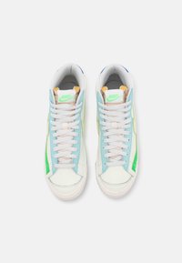 Nike-sneakers med ett vitt läderöverdrag och ljusblå och gröna accenter, platta snören och en strukturerad gummisula.