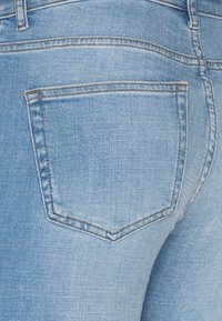 Los jeans de denim azul claro presentan un único bolsillo trasero con bordes rectos, una textura sutil y costuras en contraste a lo largo de las costuras.