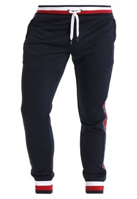 Navy joggerbroeken van zacht materiaal, met een witte trekkoord, een rood en wit gestreepte tailleband en logo-detailing langs de zijkant.