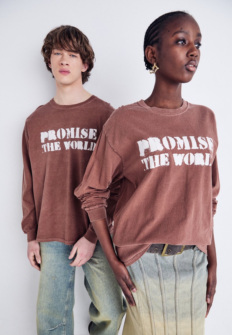 Brune langermede skjorter med teksten "PROMISE THE WORLD", kombinert med lyseblå jeans og et grønnaktig skjørt med vertikale sømmer.