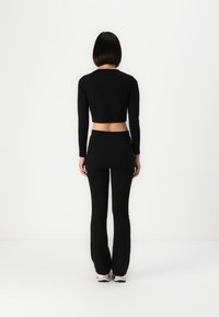 Crop top noir à manches longues avec un col rond, associé à un legging noir taille haute assorti, texture lisse, design minimaliste.