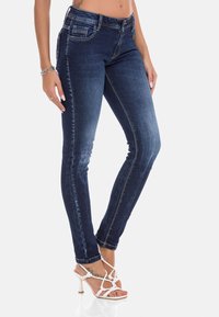 Skinny jeans in donkerblauwe denim met een lichte vervaging, voorzien van een klassiek vijf-pocket ontwerp en contrasterende stiksels, gecombineerd met witte gespsandalen.