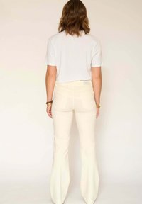 Pantalons évasés de couleur crème avec une texture lisse, taille haute et poches arrière. Associés à un t-shirt blanc uni.