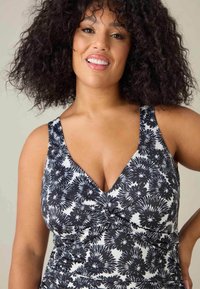 Maillot de bain floral noir et blanc avec un décolleté en V profond, de larges bretelles, des fronces au niveau de la poitrine et des détails froncés sur les côtés.