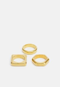 Tre anelli d'oro: una fascia rotonda liscia, una fascia quadrata e una fascia esagonale, tutti con una finitura lucida e dettagli minimi.