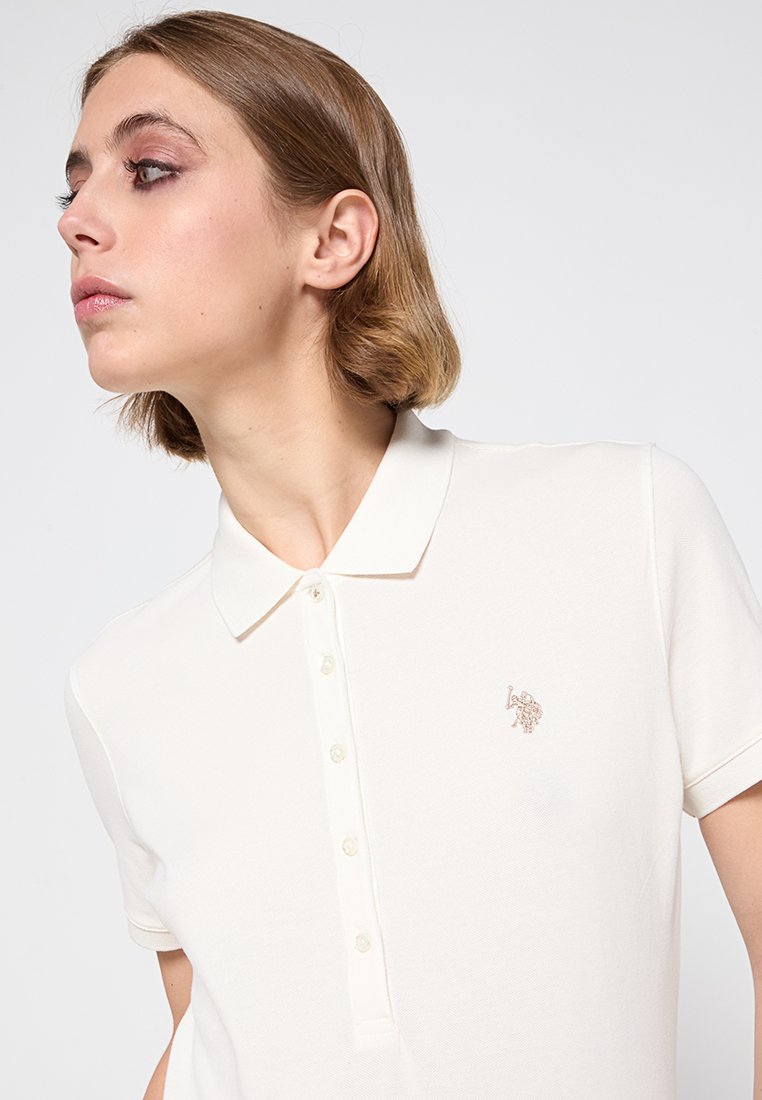 Polo bianco realizzato in tessuto morbido, con colletto classico, maniche corte e un piccolo design ricamato sul petto.