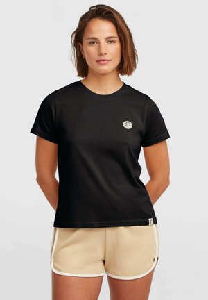 Black cotton T-shirt with short sleeves, round neckline, and a small circular logo on the chest. Worn with beige shorts featuring white trim.