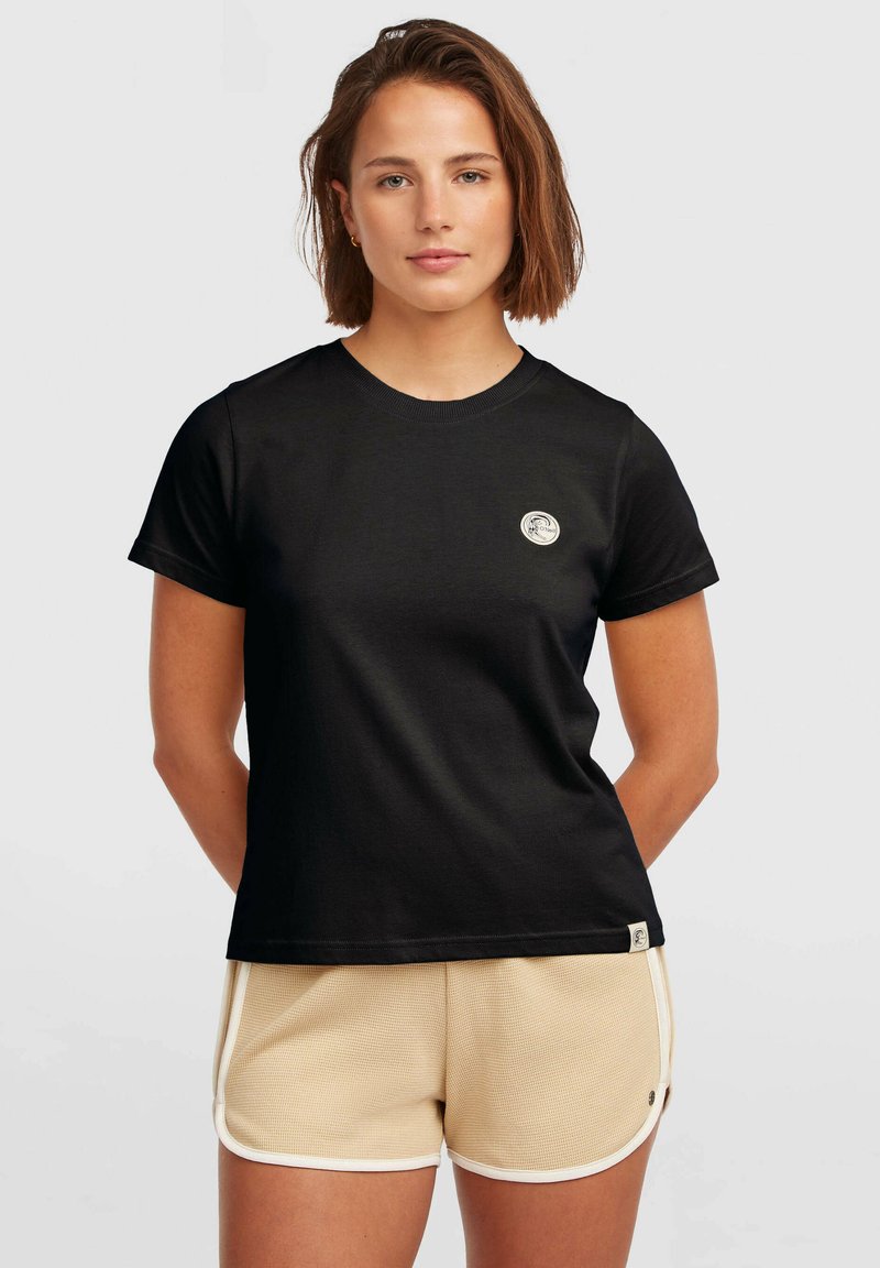 Black cotton T-shirt with short sleeves, round neckline, and a small circular logo on the chest. Worn with beige shorts featuring white trim.