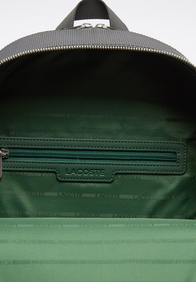 Sac à dos en tissu noir avec intérieur vert, doté d'une poche zippée et d'un logo embossé. Texture lisse et fermeture éclair durable.