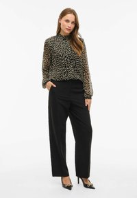 Blusa in stampa leopardata con colletto alto e polsini elasticizzati, abbinata a pantaloni neri a gamba larga e décolleté neri a punta con dettagli dorati.