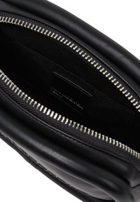 Interno di una borsa in pelle nera con una texture liscia, dettagli con cerniera e un'etichetta. La fodera è in tessuto nero con un motivo sottile.
