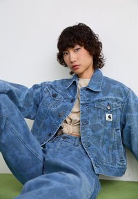 Denim jacks en broek set in vervaagd blauw met een subtiel camouflagepatroon; heeft klassieke zakken en een logo patch op de jacks.