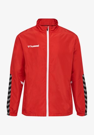 Red windbreaker jacket featuring a full zip front, high collar, and black chevron-patterned accents on the sleeves. Logo displayed on chest.