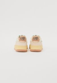 Sneakers Lacoste con tomaia in pelle color crema, dettagli verdi e suola in gomma color marrone chiaro. Presentano il marchio "L001" sul tallone. Suola testurizzata visibile.