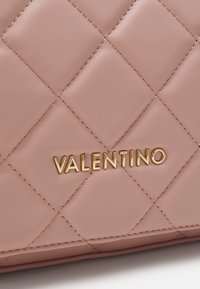Rožinė issiūta odinė rankinė su auksiniu "Valentino" logotipu. Paviršius turi lygų tekstūrą su įstrižiniais siūlų raštais.