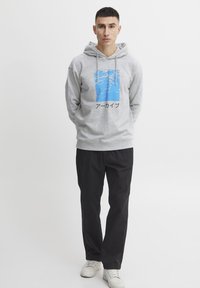Grå hættetrøje med et blåt grafisk mønster og japansk tekst, parret med sorte bukser og hvide sneakers. Designet i en afslappet pasform.