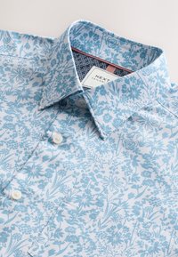 Világoskék, virágmintás ing, gombos gallérral és fehér gombokkal. Texturált belső gallérral és márkacímkével rendelkezik.