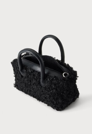 Petit sac à main noir avec un tissu texturé bouclé, deux poignées arrondies et une fermeture éclair sur le dessus, présenté sur un fond neutre.