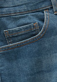 Jeans en denim de couleur bleu foncé, avec une poche arrière et des coutures oranges contrastantes le long des bords. Texture lisse, coupe standard.