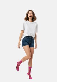 Lyserøde sokker med bananprint, båret med denimshorts og en hvid t-shirt. Sokkerne har en ribbet kant og en glat tekstur.