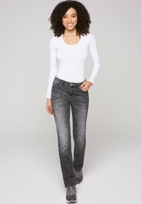Vaqueros de denim gris con un ligero desgastado, silueta ajustada y cinco bolsillos. Combinados con una camiseta de manga larga blanca y zapatillas grises.