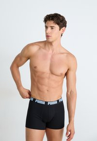 Boxeri negri cu elastic de talie cu un logo albastru. Materialul pare neted și se potrivește strâns pe o siluetă tonifiată. Design simplu și funcțional.