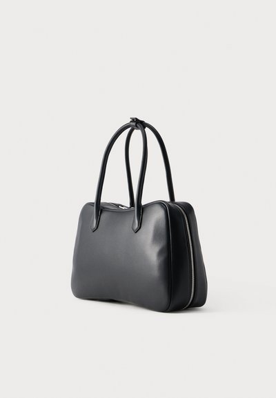 Μαύρη δερμάτινη τσάντα χειρός με διπλές λαβές και εμφανές ασημί φερμουάρ στο πλάι, εμφανιζόμενη σε απλό λευκό φόντο.